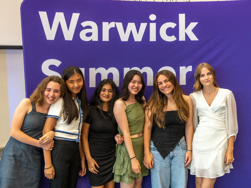 Students smiling next to a Warwick summer sign
