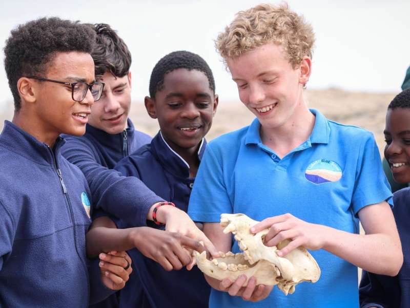 Students smiling whilst examining a brown hyena skull outside