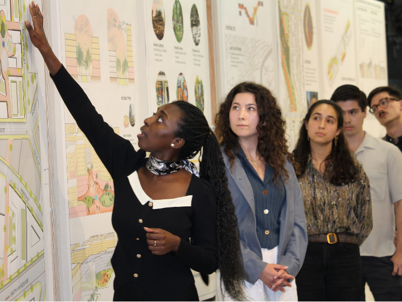 Students standing in front of their pin-ups, one is explaining