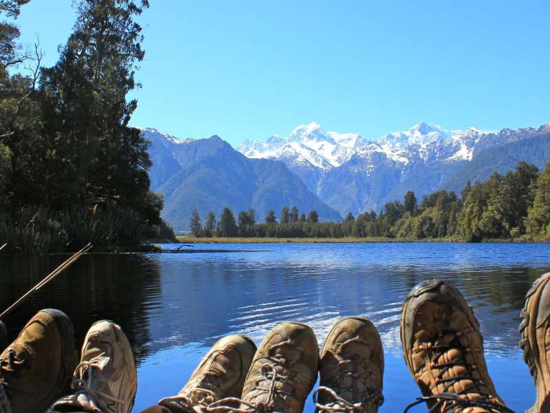 students with their boots in the air in front of a lake and mountains