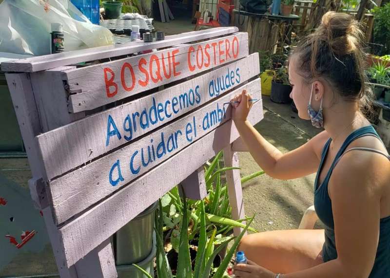 Teen volunteer painting a wooden sign with an environmental message.