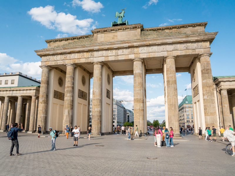 The Brandenburg Gate in Berlin with tourists walking around the historic monument on a sunny day.