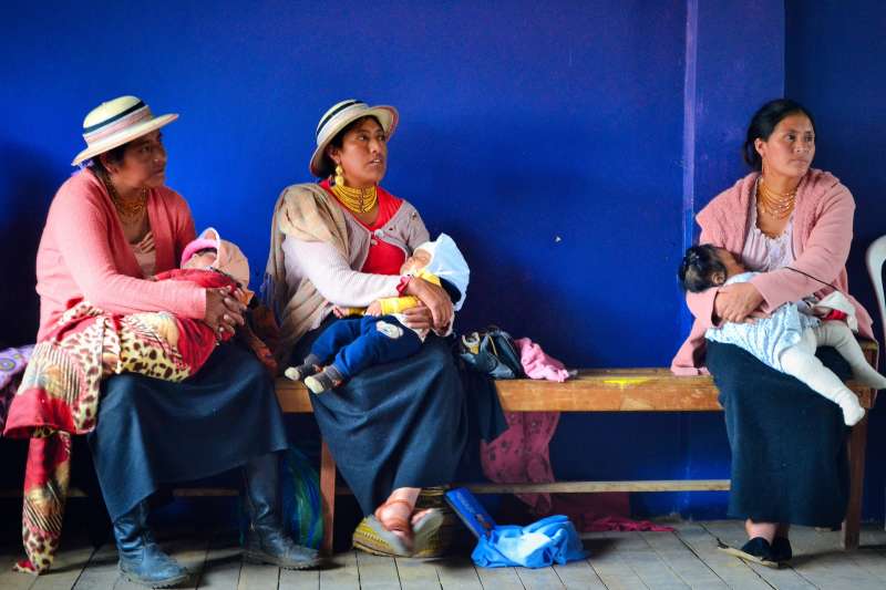 Three indigenous women south America in traditional dress sitting with babies