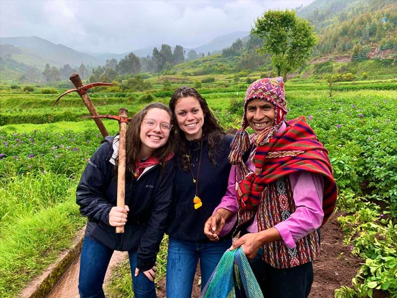 Three people smile together in a lush, terraced field beneath misty mountain.
