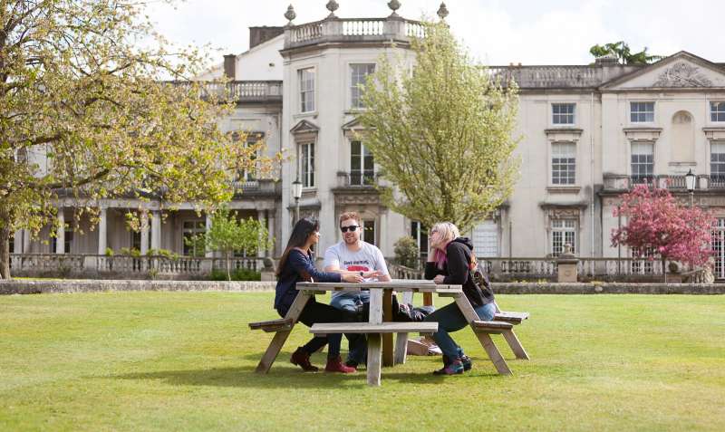 Three students on a bench outside Grove House, University of Roehampton. 