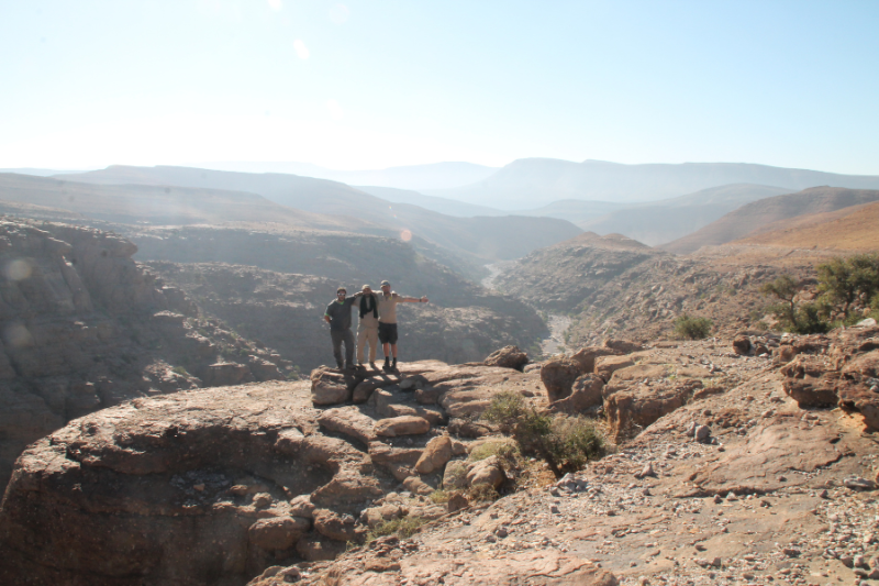 three travelers on a viewpoint overlooking a dramatic canyon landscape