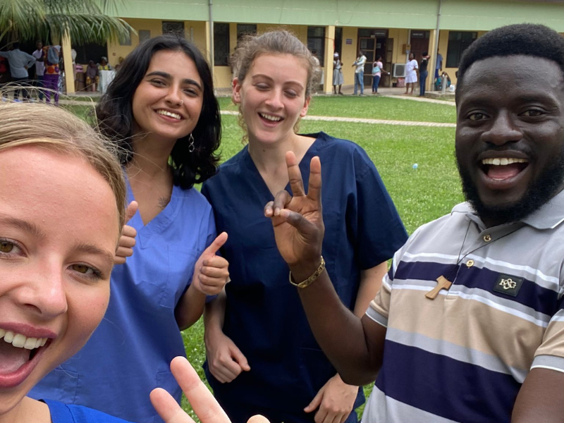 Three volunteers smile in their scrubs with a staff member, who shows a peace sign to the camera. 