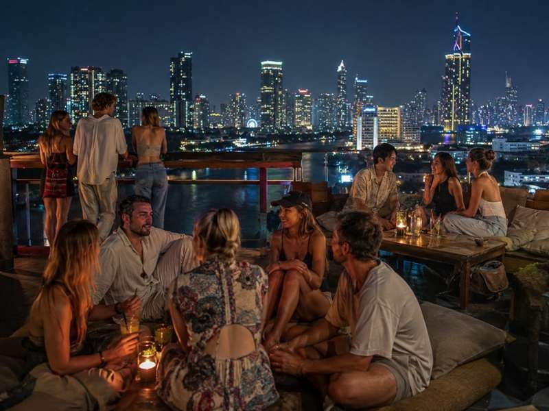 Travellers socialising at a rooftop bar overlooking Bangkok