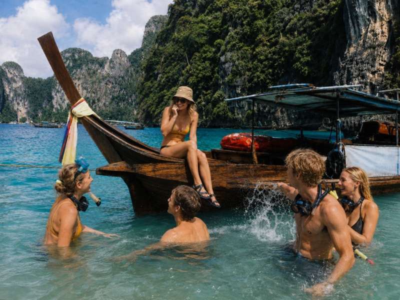 Travellers swimming beside a longtail boat in Thailand
