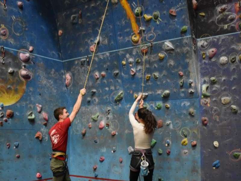 Two dublin students standing in front of a rock climbing wall holding on to rope and smiling