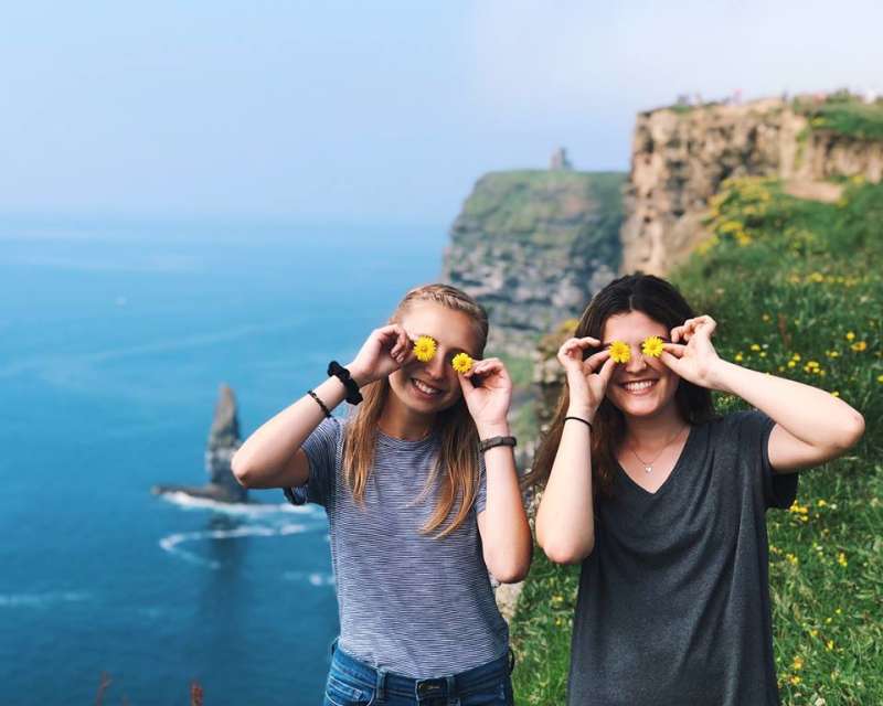 Two girls standing on edge of a cliff with yellow flowers on eyes 
