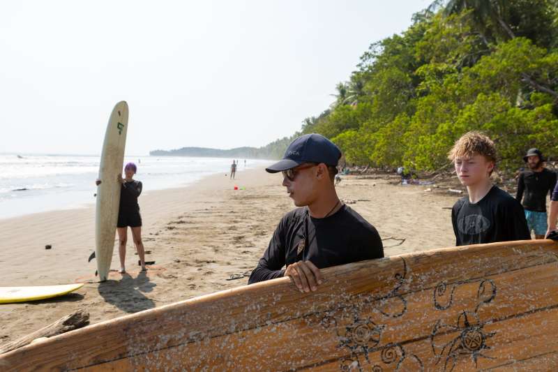 Two people carry surfboard towards ocean