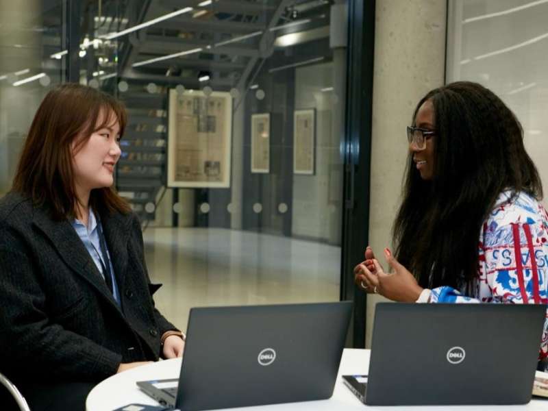 Two people seated at a table with laptops in a modern office space.