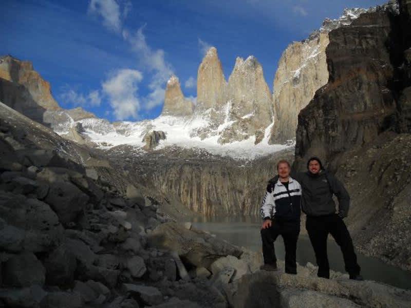 Two people standing on rocks, admiring a majestic mountain in the background.