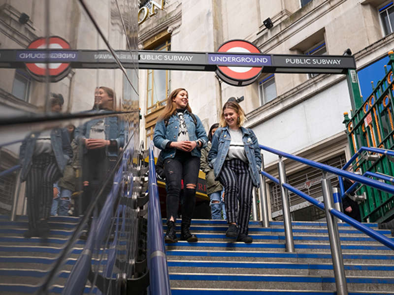 Two students walk down steps with a London Underground sign above them