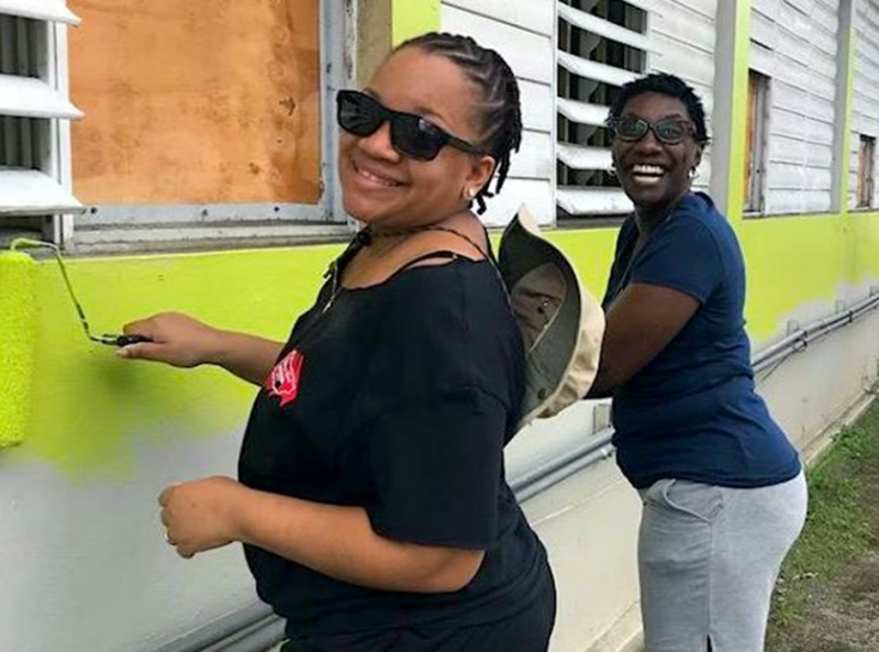 Two volunteers smiling while painting an exterior wall.