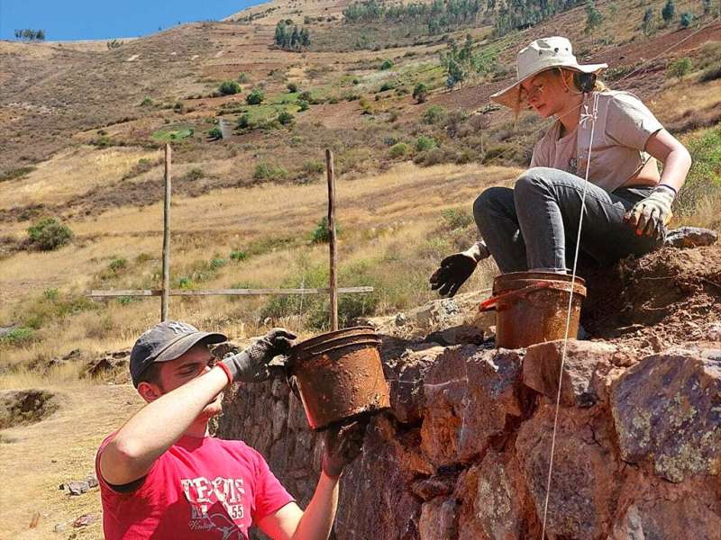 Two volunteers work together to build a stone wall on a sunny hillside in Peru.