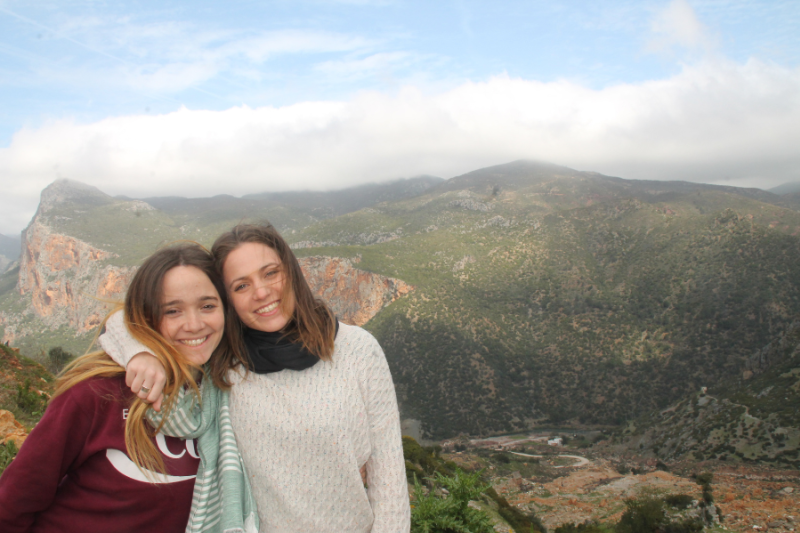two women posing for a photo against a scenic, mountainous backdrop