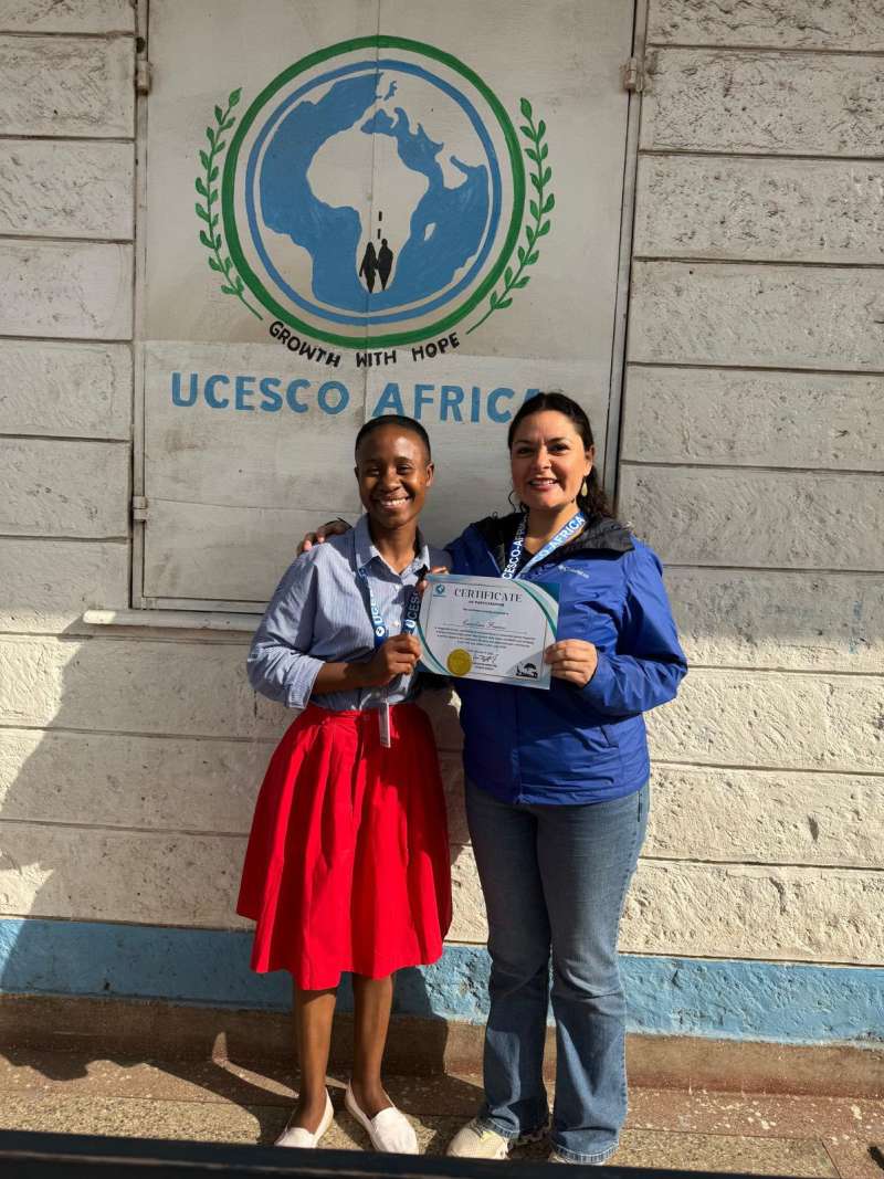 UCESCO volunteer holding a certificate, standing beside a local woman