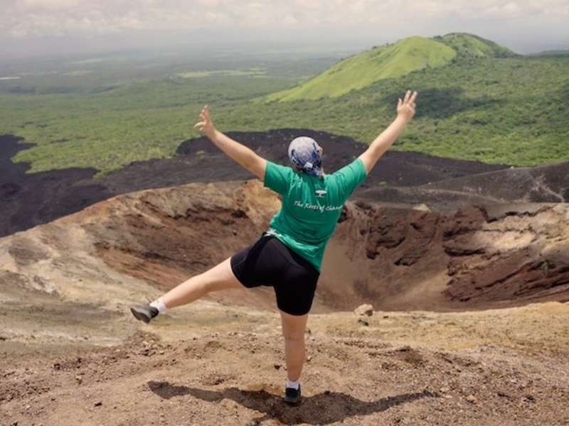 Volunteer posing in front of volcanic crater during volcano adventure