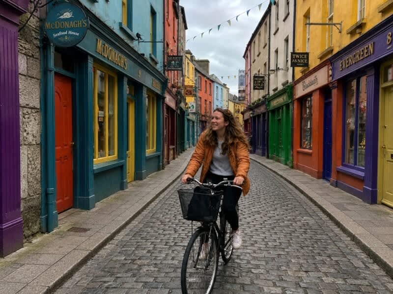 Young woman cycling through a colourful street in Galway